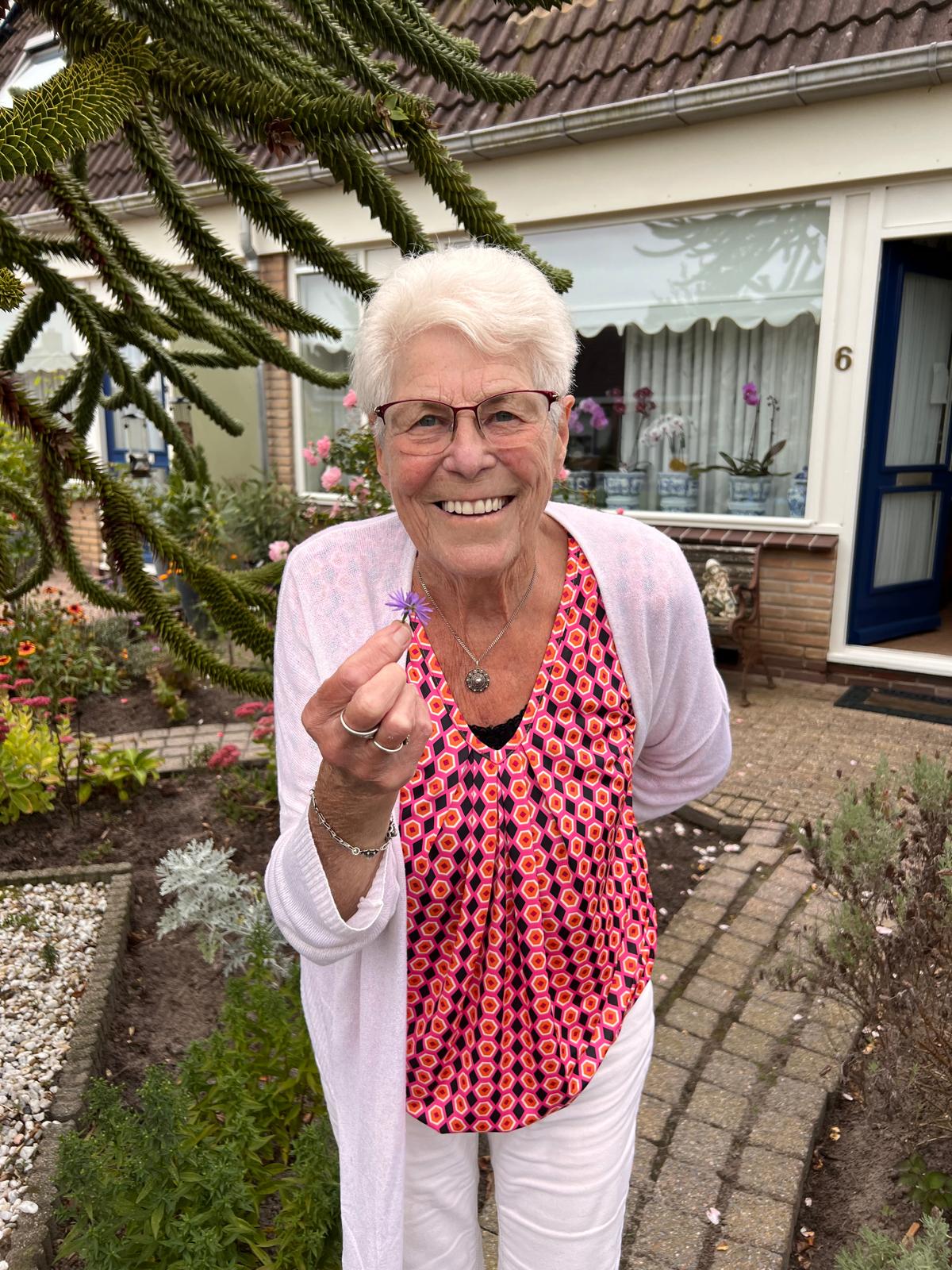 Oma, het boegbeeld van TOEK, met een bloemetje in haar hand voor haar huis